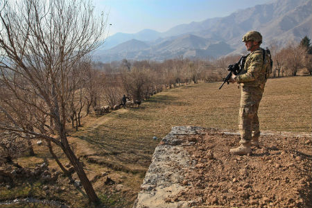 A soldier on deployment in Afghanistan. In the distance, a shepherd herds his sheep.