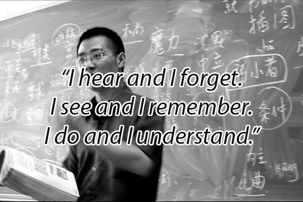 photo of a chinese teacher reading in front of class with a Confucius quote built over the top of the image reading: "I hear and I forget. I see and I remember. I do and I understand"