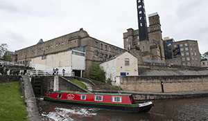Canal boat waiting at lock by a factory with chimney tower and warehouses by side of canal