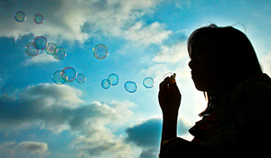 Silhouetted girl blowing bubbles against a blue sky