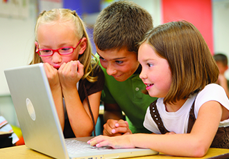 Three primary school children grouped around a laptop