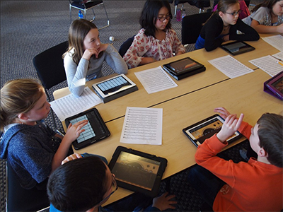 A group of junior school children sat around a table, each with a table computer