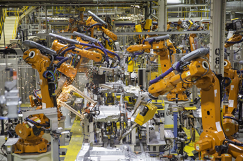 A photograph of the Landrover Discovery production line in modern times. The photo is in colour and shows to paired lines of orange machines that are moving their top halves in different directions. 