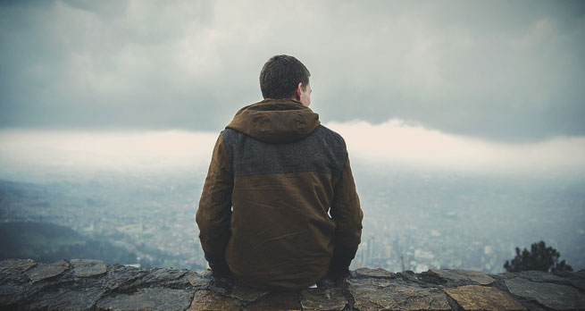 Man looking out over a town as clouds gather above him