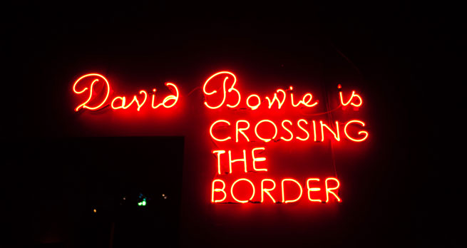 A neon sign reading David Bowie is crossing the border
