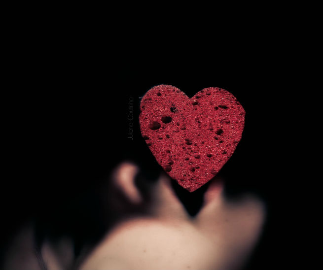 A red heart held against a black background
