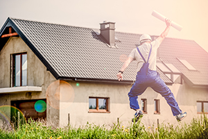 Builder jumps in the air with joy with paper in his hand, in front of a house and a sunny sky