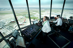Two air traffic controllers look out from Heathrow air traffic control tower over the runways. 