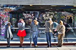 Young people stand in front of a skatepark full of graffiti. 