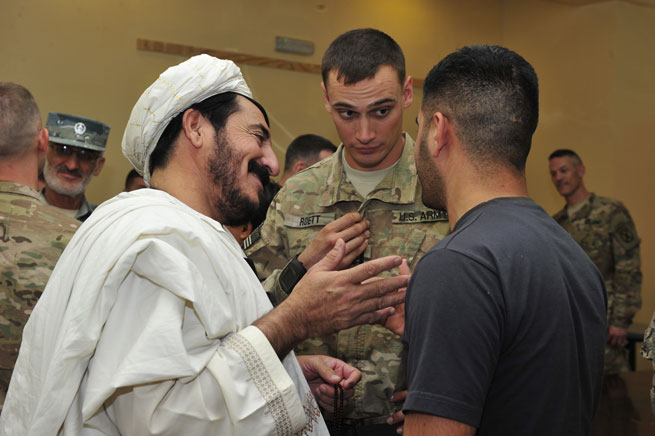Dand District Governor Hashim Agha (left) greets U.S. Army Capt. Scott Roett from Train, Advise and Assist Command - South (TAAC-S) and an interpreter at a Kandahar Airfield security shura held at the Joint Regional Afghan National Police Center (JRAC) in Kandahar, Afghanistan June 27, 2015.
