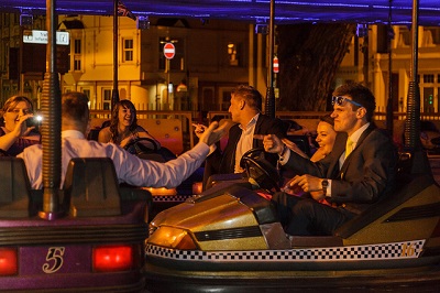 Young people in formal suits and dresses on bumper cars, challenging each other