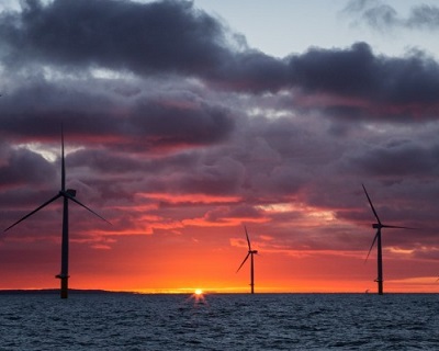 The sun rises behind an offshore wind farm