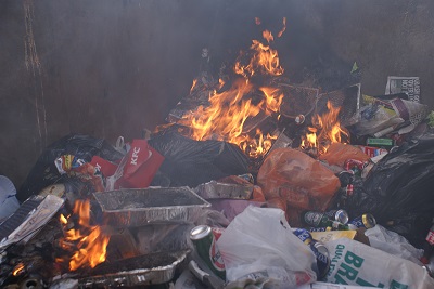 A burning pile of garbage in a skip, giving off large amounts of thick black smoke 