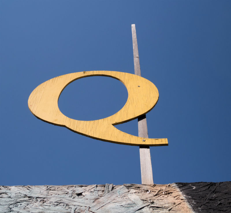 The letter q on a dowel against the blue sky