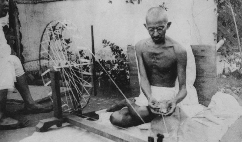 Landscape image of Gandhi spinning, black and white.