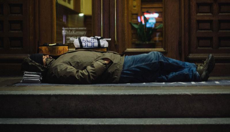 A homeless man sleeping on newspaper and concrete
