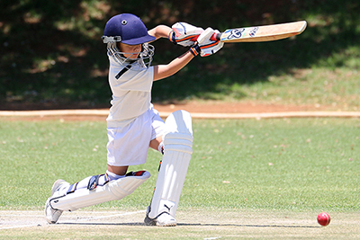 Child playing cricket, mid-strike. Under the sun