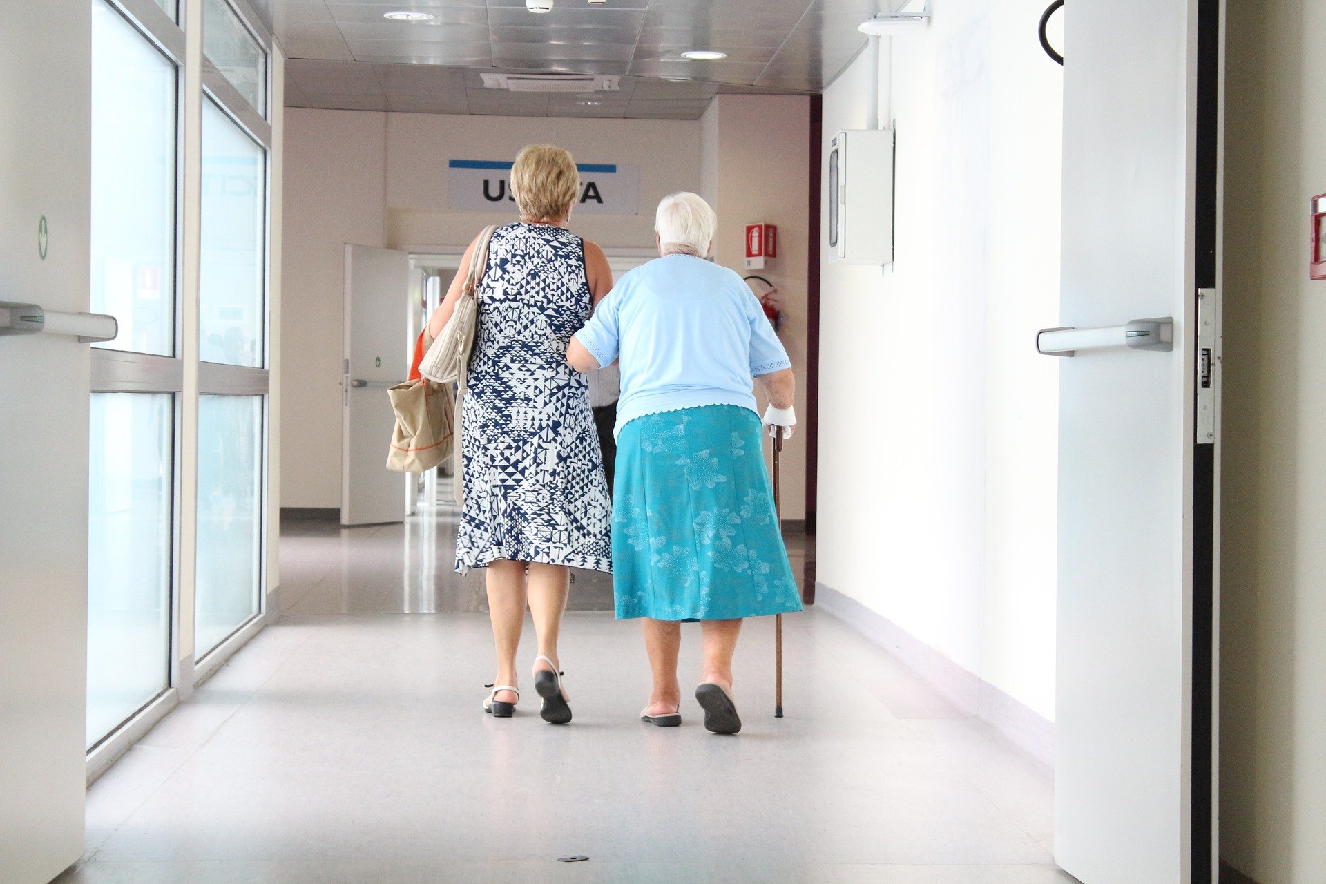 Middle aged woman aiding her elderly mother down hospital corridor