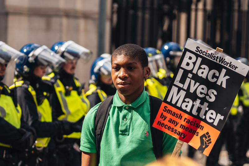 Young man with BLM banner posing in front of Police officers