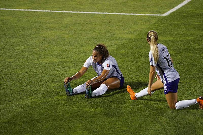two female footballers stretching on the pitch