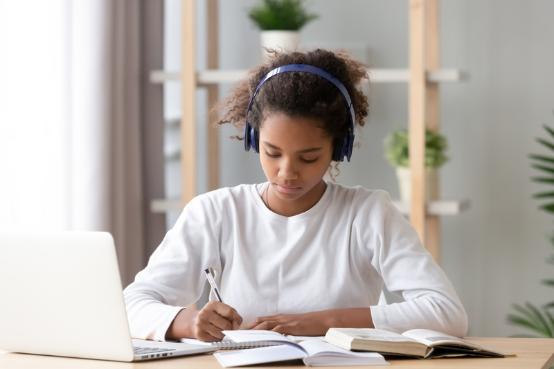 teen girl wearing headphones writing notes studying