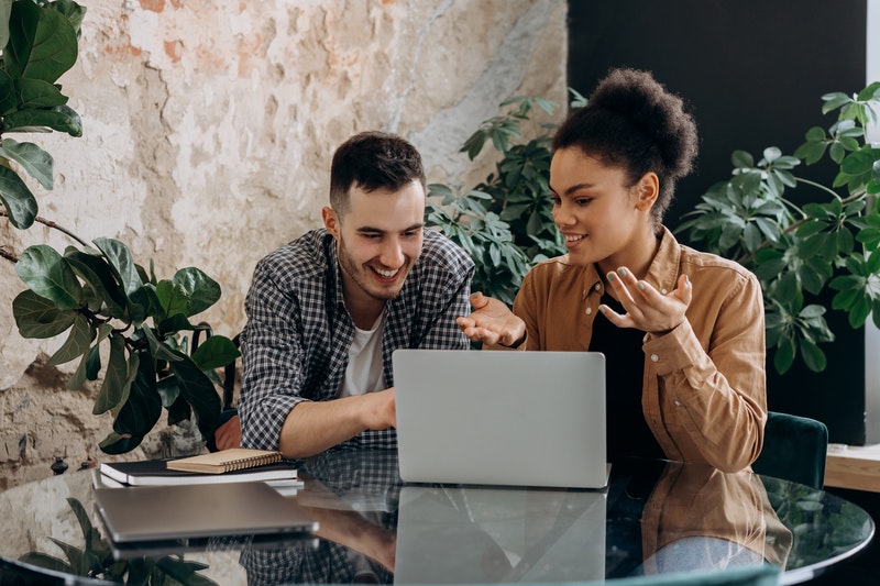 man and woman talking while using laptop