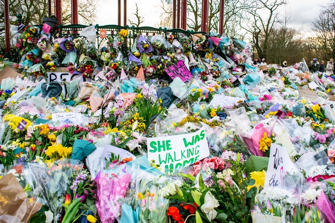 A large amount of flowers laid on the ground with a sign saying 'She was walking home'