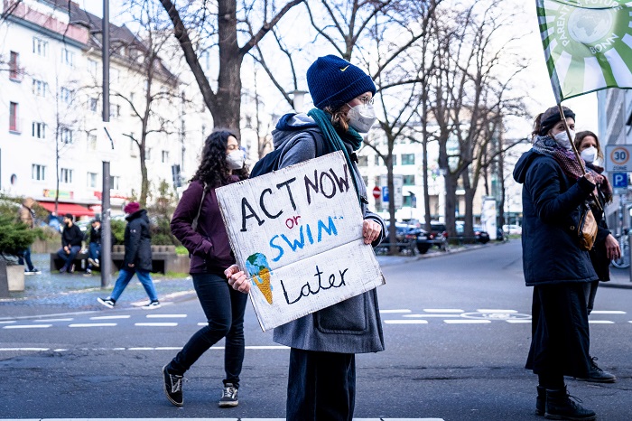 A person holding a sign which says 'Act now or swim later'