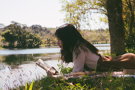 South Asian woman reading a book in nature, surrounded by water