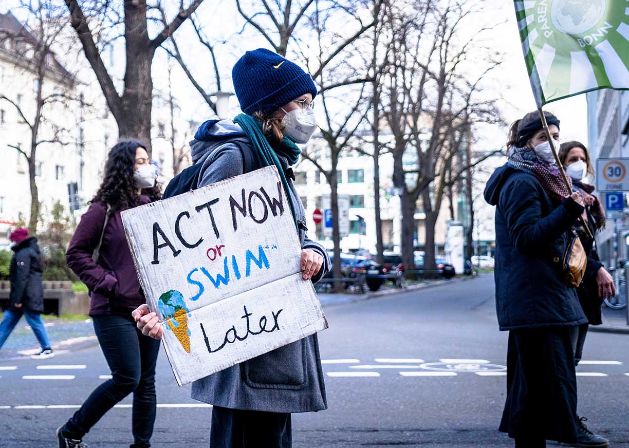 Woman protesting with sign saying 'Act now or Swim later'