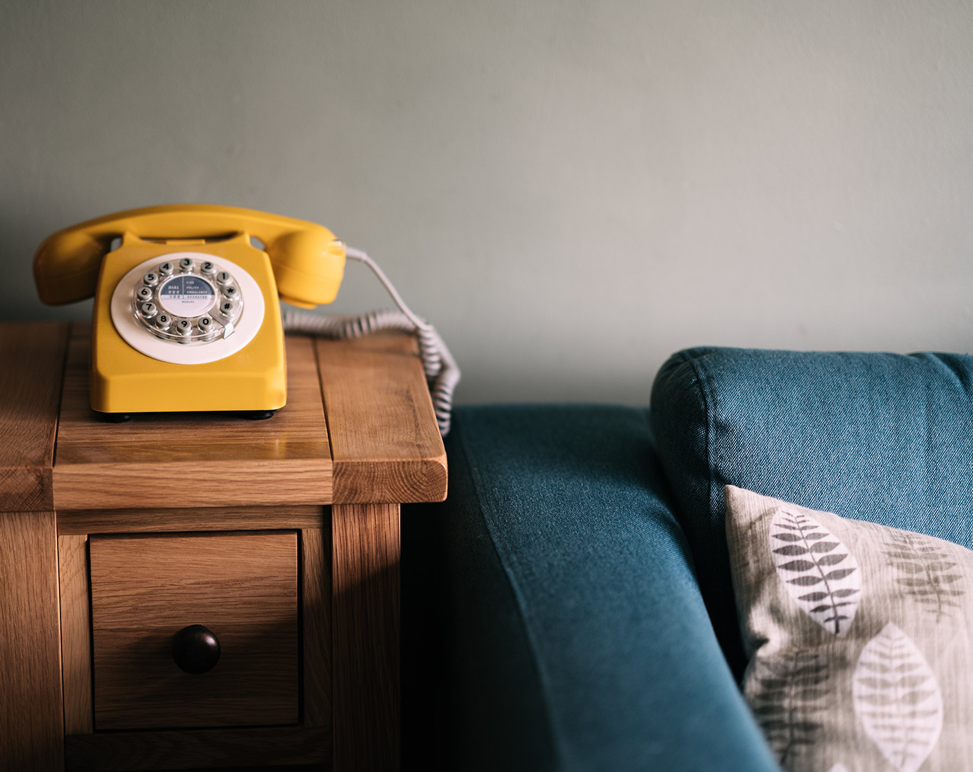 A photo of a yellow rotary telephone near a blue sofa.