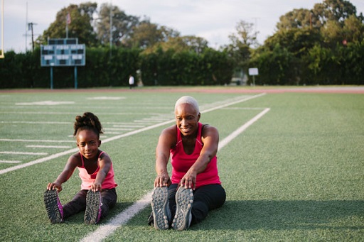 Image of young girl and her grandmother stretching on a sports pitch