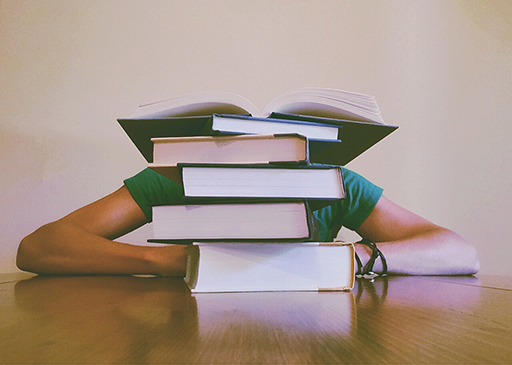 A photograph of a person hiding behind a stack of books.