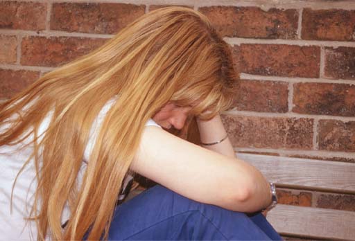 A photograph of a person sat on the floor with their knees up and their head in their hands.