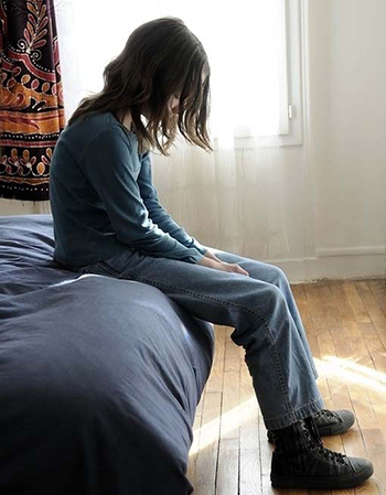 Sad 12 year-old young person sitting on their bed.