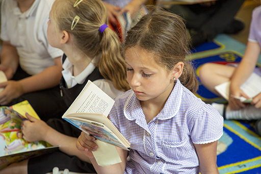 A young girl sat on the floor in class reading.