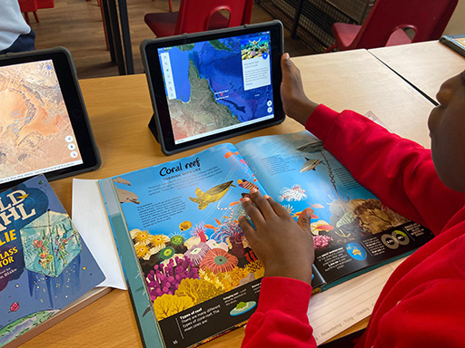 A school child looking at a tablet and a book on coral reef
