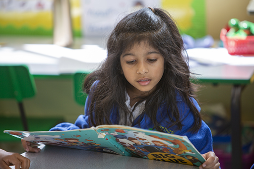 A schoolgirl at a table reading a book.