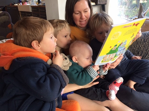 A parent reading to her four young children on the sofa.