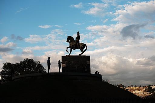 A photograph of a statue featuring a man on a horse, situated on a hill.