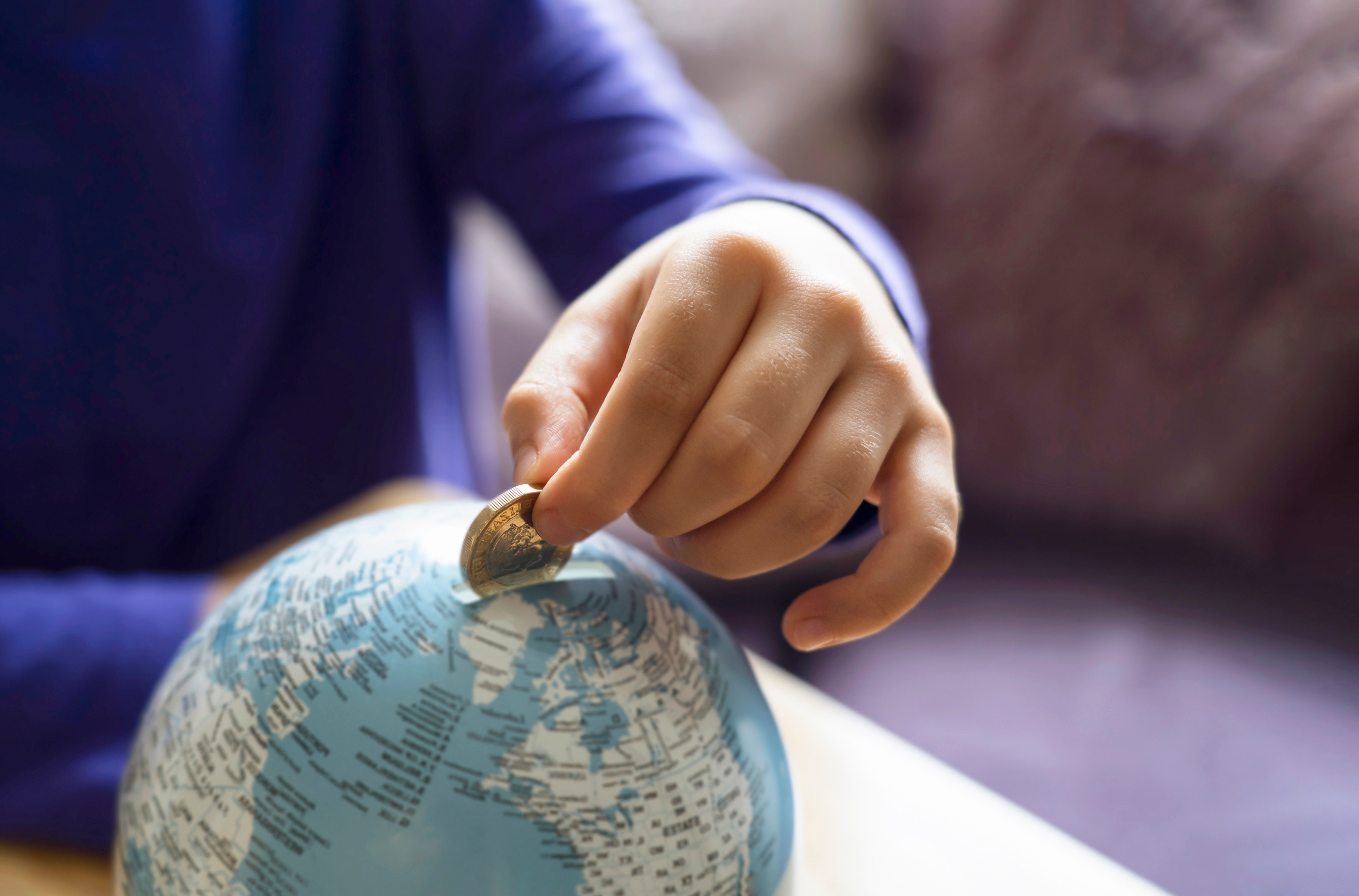 Photo of a person putting a coin into a globe piggy bank