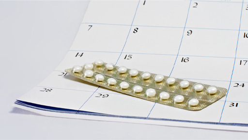 The image shows a packet of contraceptive pills on top of a calendar.