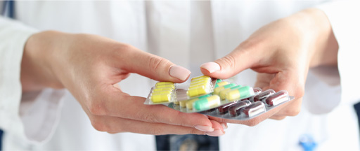 The image shows a female in a lab coat holding packets of pills.