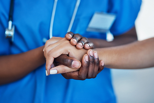 A close-up of a nurse holding a patient’s hand.