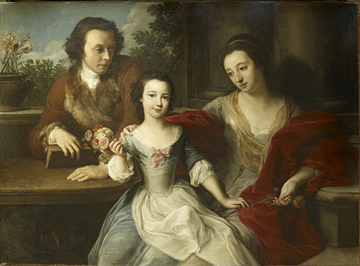 This triple portrait shows three seated figures in the foreground: the man, Thomas Barrett-Lennard, sits behind a table to the left; his wife, Anna Marie, sits on a stone bench to the right; both gaze at their daughter, Barbara Anne, who is central to the image. Barbara Anne is a young girl with very pale skin and dark eyes; her dark hair is tied back. She wears a green-blue gown with a white apron and a pink bow at the centre of the neckline. She looks directly outwards and smiles. Her left hand rests on her mother’s lap; in her right hand, she holds a bunch of pink, red and white carnations. Her mother has a pale oval face and dark hair; she wears a white silk gown and a shawl of red cloth. Her right arm extends behind her daughter and rests on the table. Thomas Barrett-Lennard sits in a slightly raised position to the left of his daughter. He is also pale-faced and dark-haired. He wears a dark red jacket trimmed with fur. Behind him, positioned on the ledge of a window opening, is a brown vase of pale flowers. Dark foliage with white clouds and blue sky is pictured through the opening to the right.