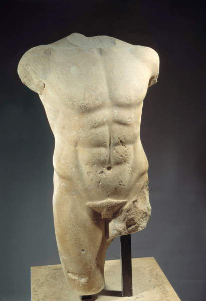 This colour photograph in portrait format features a naked torso sculptured in pale marble. The abdominal muscles are realistically rendered. The head and arms are missing; so, too, is much of the genitalia and the top of the thigh on the right-hand side of the image. The torso is lit from the right, against a dark background. It is attached to a square stone plinth by dark metal posts.