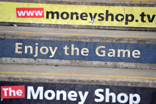 A photograph of steps at a ground with adverts for the money shop.