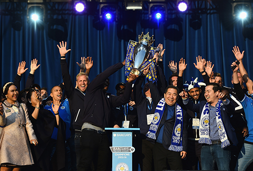 A photograph of the two Leicester City owners holding up the Premier League trophy among a crowd of players.
