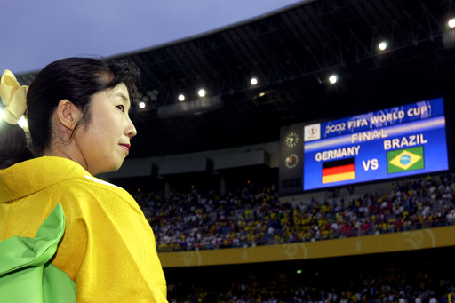 A photograph of a woman in traditional Japanese costume in a crowded stadium.