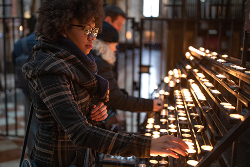 This is a colour photograph of a woman lighting a candle in a church.